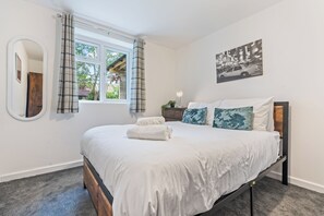 A bedroom with a bed, a window with curtains, a bedside table with a lamp, and a wall-mounted mirror. - Private and Beautiful 1BR Apartment near South Park,Churchill Hospital, Oxford. (Oxford)