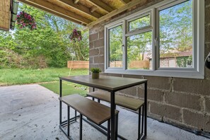 An outdoor patio with a table and benches, a hanging flower basket, and a view of a backyard with a wooden fence. - Private and Beautiful 1BR Apartment near South Park,Churchill Hospital, Oxford. (Oxford)