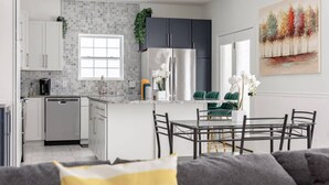 Una cocina moderna con armarios blancos, un refrigerador de acero inoxidable y un comedor con mesa y sillas de vidrio.