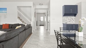 Una sala de estar moderna con un sofá seccional gris, una mesa de comedor con sillas y una cocina con armarios oscuros y salpicadero.