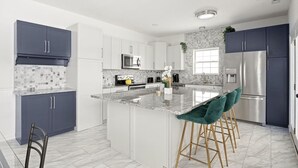 Una cocina moderna con armarios grises, una isla central con taburetes altos, un refrigerador de acero inoxidable y un microondas.