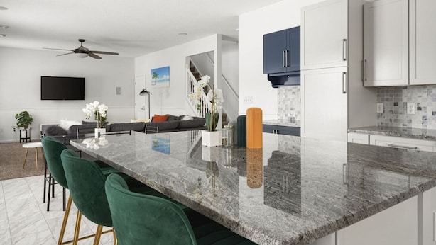 Una cocina moderna con encimera de mármol, sillas verdes y un rincón de comedor con sofá.