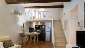 Un espacio habitable compacto con kitchenette, comedor, sofá, televisor y escalera que sube a un nivel superior.