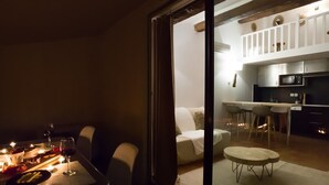 Un comedor acogedor con una mesa lista para dos, un sofá, y una cocina visible a través de una puerta abierta.