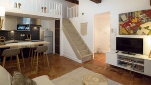 Una cocina moderna con comedor, una escalera y una sala de estar con televisor y estanterías.