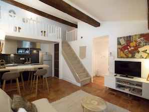 Une cuisine moderne avec un coin repas, un escalier et un salon équipé d’un téléviseur et de bibliothèques.