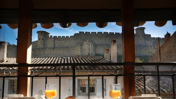 Desayuno con cruasanes, zumo de naranja y vistas a una muralla de castillo.