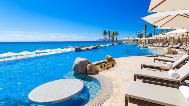 A pool area with lounge chairs and umbrellas, a clear blue sky, and a view of the ocean. - Stay at the 5-Diamond Villa la Valencia (San Jose del Cabo)
