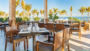 An outdoor dining area with tables and chairs, palm trees, and a view of the ocean. - Stay at the 5-Diamond Villa la Valencia (San Jose del Cabo)