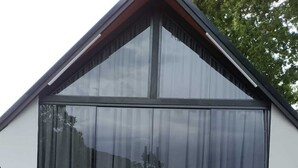 Un edificio moderno con un amplio frente de vidrio, una terraza de madera y un suelo de grava.