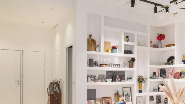 A modern, white-themed living space with a large white shelving unit filled with various decorative items and a cozy seating area with a striped cushion. - Sublime artist's loft in Montreuil ideal for families. (Montreuil)