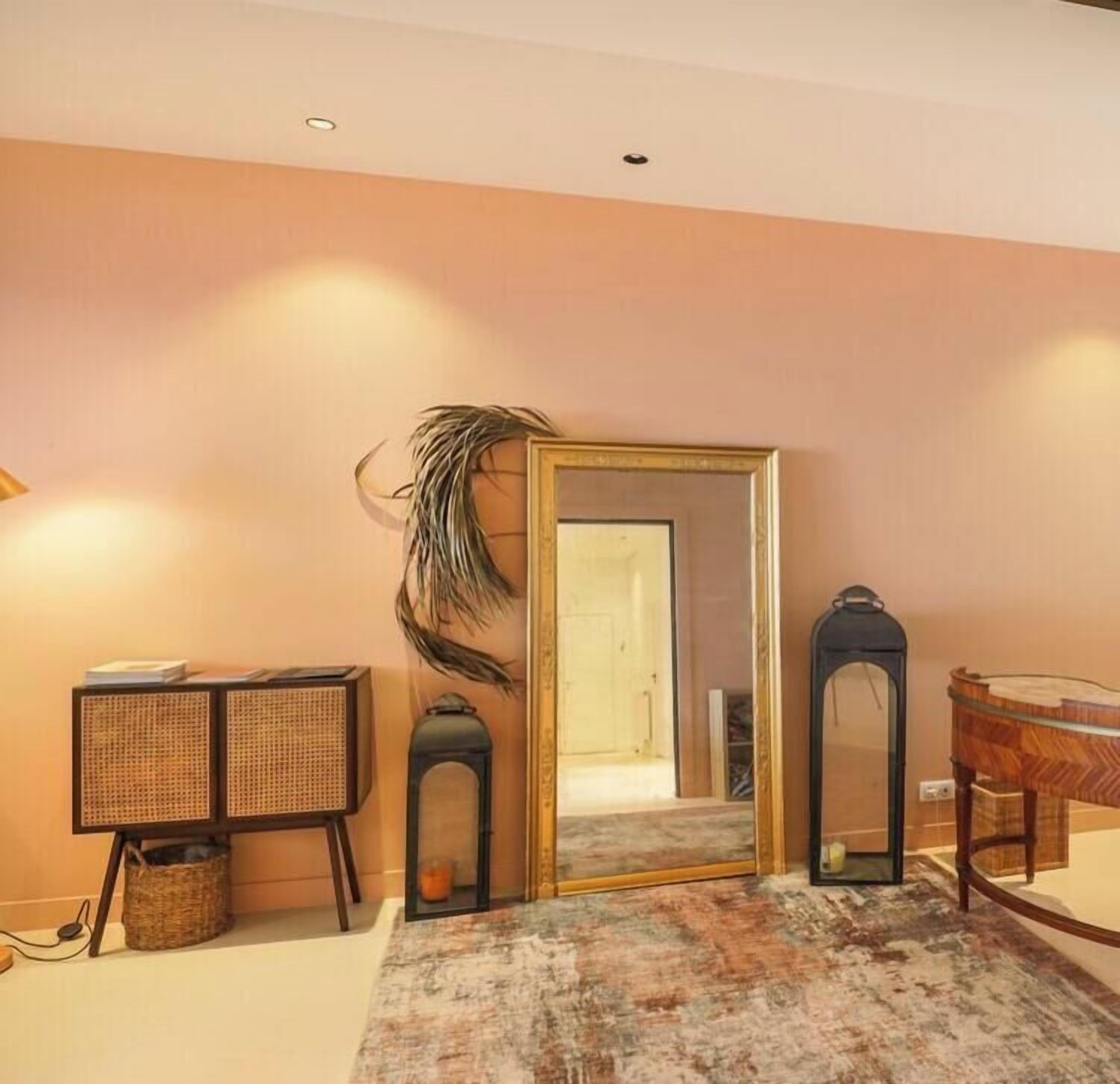 Une pièce avec un grand miroir, un panier en osier, une petite table et une plante décorative.
