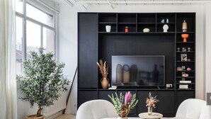 A modern living room with a large flat-screen TV, a black entertainment unit, two white armchairs, and a potted plant. - Sublime artist's loft in Montreuil ideal for families. (Montreuil)