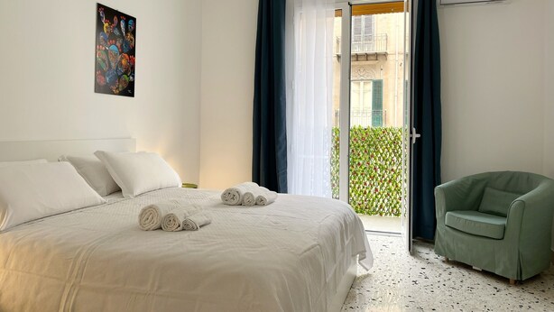 Una habitación de hotel con cama, una silla verde, balcón con vistas y aire acondicionado.