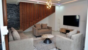 Un salon moderne comprenant un ensemble de canapés, une table basse, un téléviseur et un mur avec des lambris en bois.