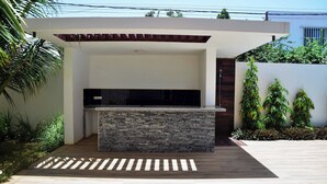 Un espace cuisine extérieur moderne, doté d’un plan de travail en pierre et d’appareils électroménagers intégrés.