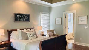 A bedroom with a large bed, bedside tables, a bench, and a window with blinds. - Masters Rental 4-bedroom house in Golf Course Community (Evans)
