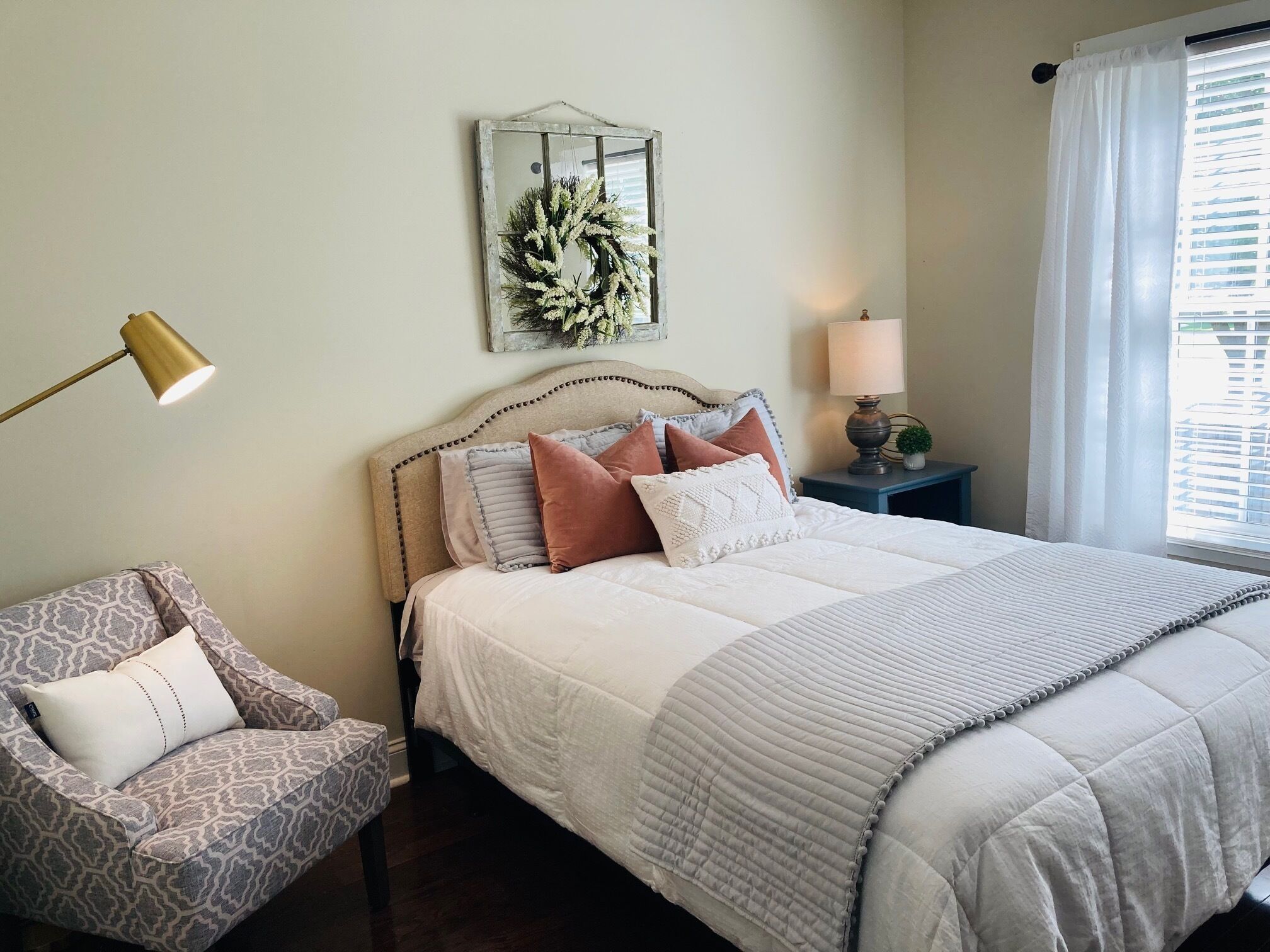 A bedroom with a bed, a chair, a nightstand, a lamp, and a window with curtains.