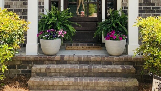 A brick house with a front door, two potted plants, and a welcome sign. - Masters Rental 4-bedroom house in Golf Course Community (Evans)