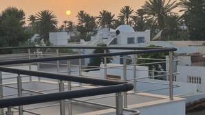 Eine Dachterrasse mit Metallgeländern, ein weißes Gebäude im Hintergrund und Palmen.