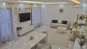 Ein modernes Wohnzimmer mit Marmorboden, einem großen Esstisch, einer Sofagarnitur und einem an der Wand befestigten Fernseher.