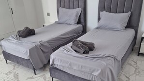Zwei Betten mit grauen Kopfteilen und passender Bettwäsche, ein Kleiderschrank und ein Fliesenboden.