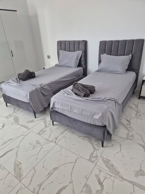 Two beds with grey headboards and matching bedding, a wardrobe, and a tiled floor. - Villa DALISSA with heated pool - Midoun - Djerba - TUNISIA (Djerba Midun)