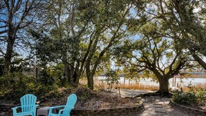 A patio area with two blue Adirondack chairs, a small table, and a tree-lined view of a body of water. - Bayfront backyard with a dock, 3BR, Dogs Welcome! (Norfolk)
