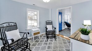 A room with a stone-patterned floor, a black metal bench with a white cushion, a black chair with a white cushion, a white desk, and a wooden table with a plant. - Bayfront backyard with a dock, 3BR, Dogs Welcome! (Norfolk)