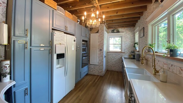 Una cocina con armarios azules, un refrigerador, un horno, un lavamanos y una ventana con vistas.
