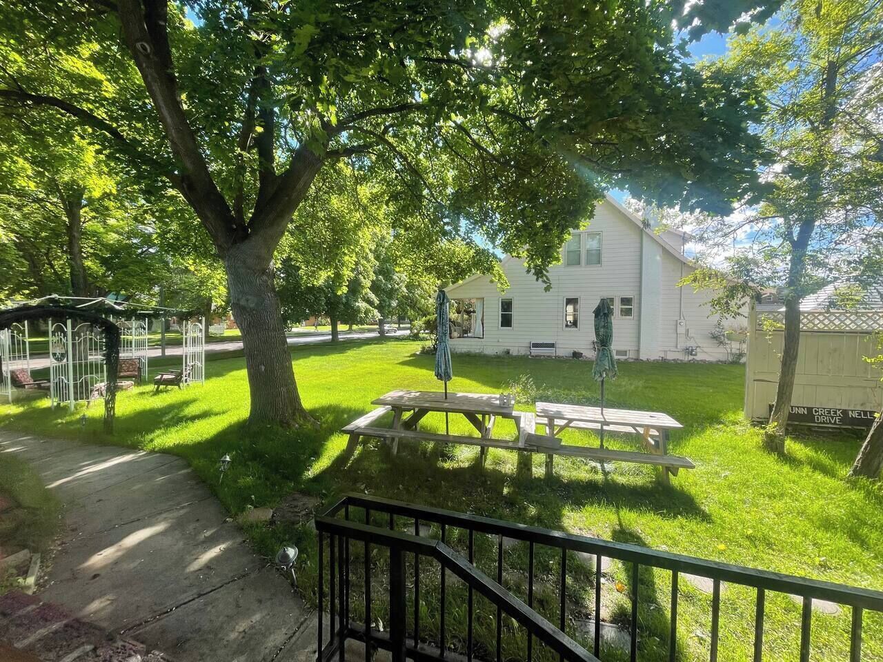 A white house with a covered patio and picnic table in a grassy yard.