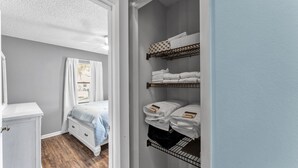 A bedroom with a bed, a white dresser, and a built-in closet with multiple shelves for storage.