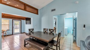 A dining area with a wooden table and benches, light blue walls, and a view of a laundry room through an open door.