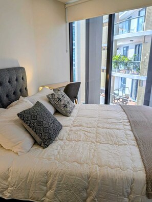 Un dormitorio con una cama grande, un cabecero tapizado gris y vistas a un balcón con mobiliario exterior.