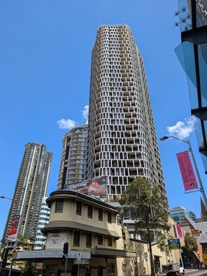 A tall, cylindrical building with a grid-like facade, surrounded by other high-rise buildings. - Premium Unit w/ Rooftop Pool in the Heart of Brisbane (Brisbane City)