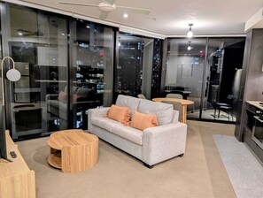 A modern living room with a grey sofa, a round wooden coffee table, and a glass partition with a city view. - Premium Unit w/ Rooftop Pool in the Heart of Brisbane (Brisbane City)