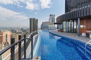 Una piscina infinita en la azotea con vistas a la ciudad, arquitectura moderna y una zona de terraza de madera.
