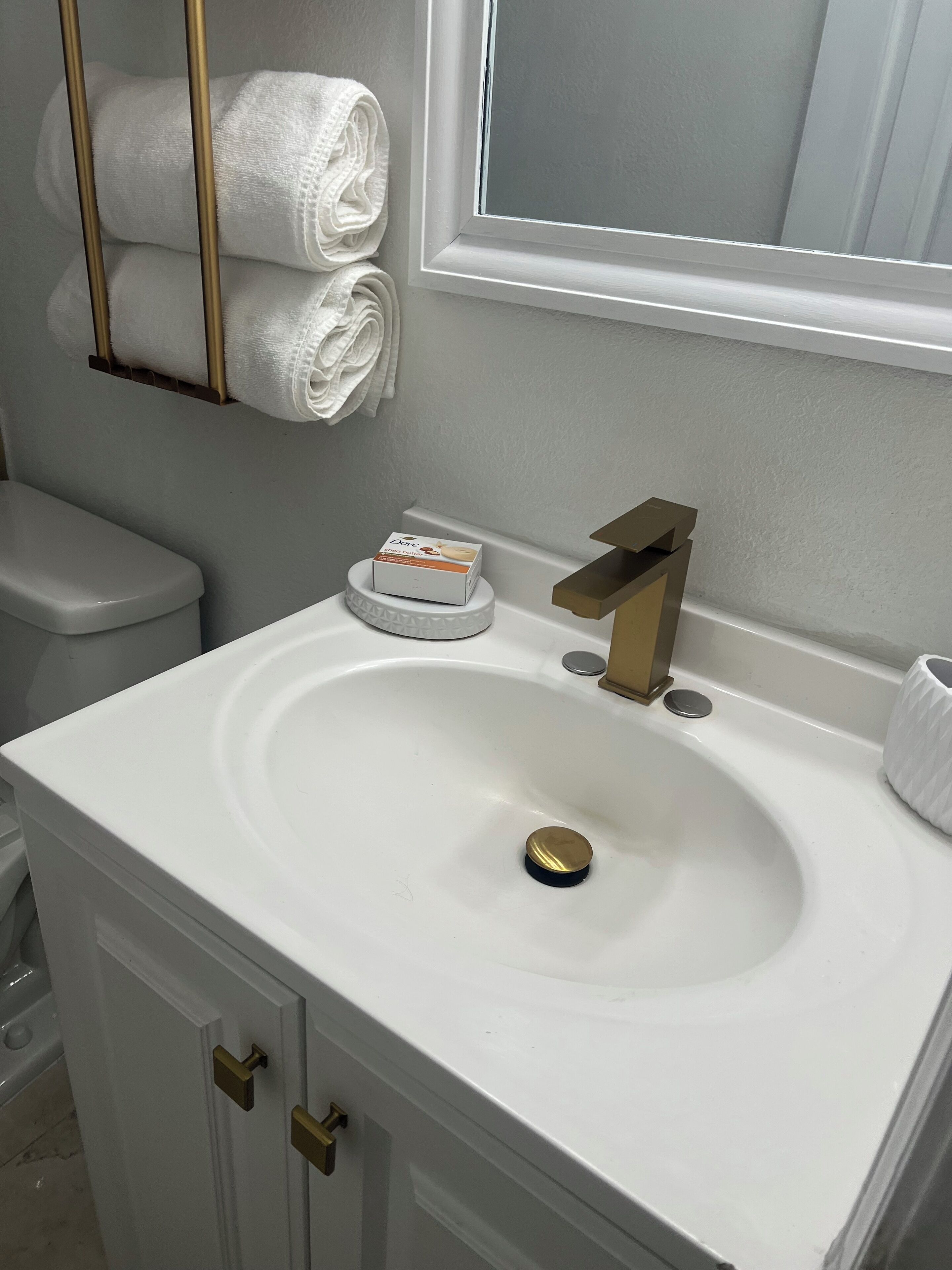 A bathroom with a white sink, gold faucet, and a towel rack with folded towels.