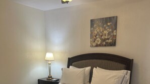A neatly made bed with white linens, a dark wooden headboard, a bedside lamp, and a ceiling fan.