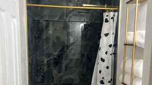 A bathroom with a glass-enclosed shower, a white toilet, and a gold-framed towel rack.