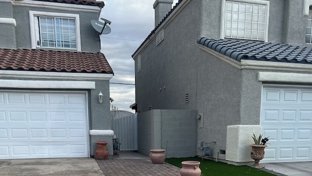 A residential driveway with a concrete path, potted plants, and a garage door.