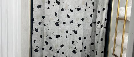 Un baño con inodoro blanco, cortina de ducha estampada y espejo con marco dorado.