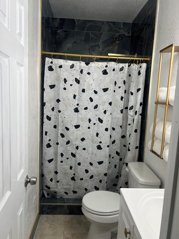 Un baño con inodoro blanco, cortina de ducha estampada y espejo con marco dorado.