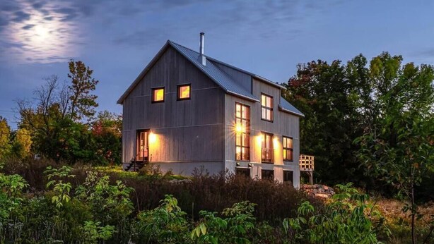 A two-story wooden house with a sloped roof, multiple windows, and a visible chimney.