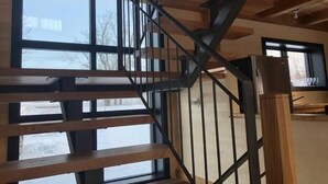 A wooden staircase with metal railings, large windows, and a view of the outside.