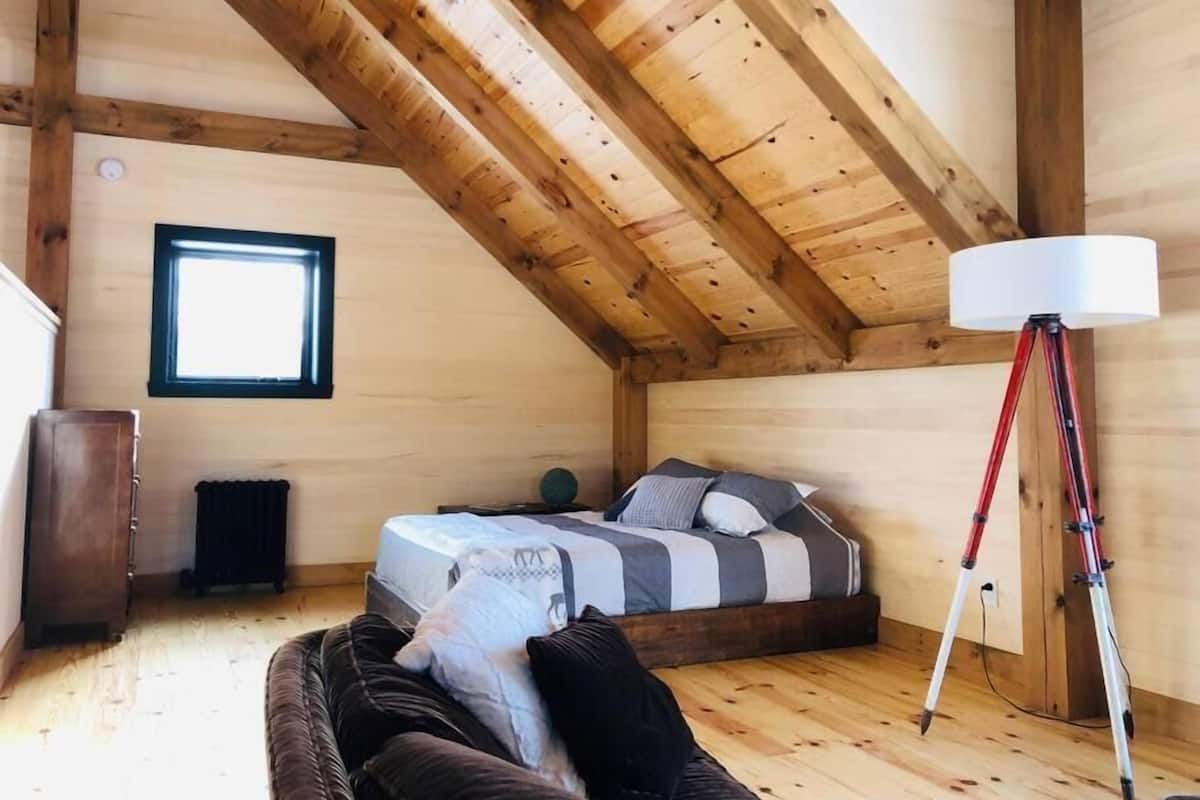 A cozy attic bedroom with a sloped ceiling, a single bed with striped bedding, a floor lamp, and a window.