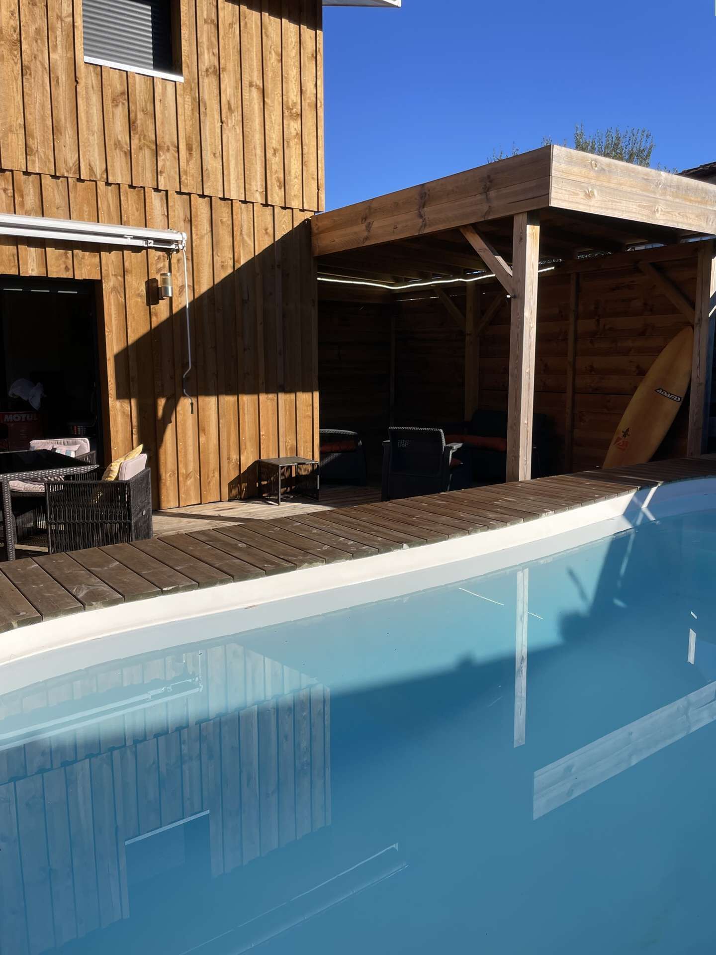 Un bâtiment en bois doté d’une piscine, d’un espace extérieur aménagé et d’une planche de surf.