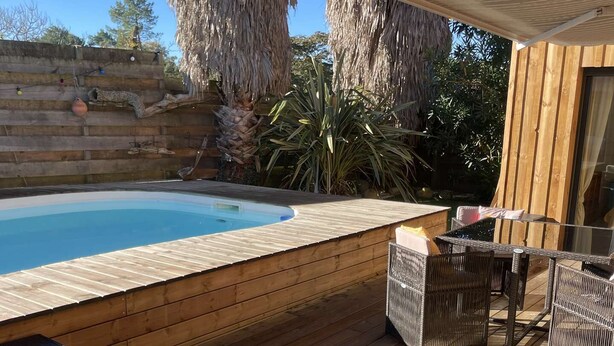 A wooden deck with a pool, wicker furniture, and tropical plants. - Villa d'Huchet (MOLIETS ET MAA)