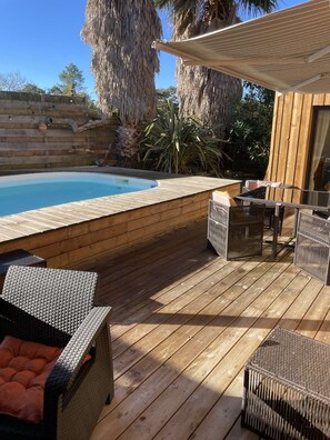 A wooden deck with a pool, wicker furniture, and tropical plants. - Villa d'Huchet (MOLIETS ET MAA)