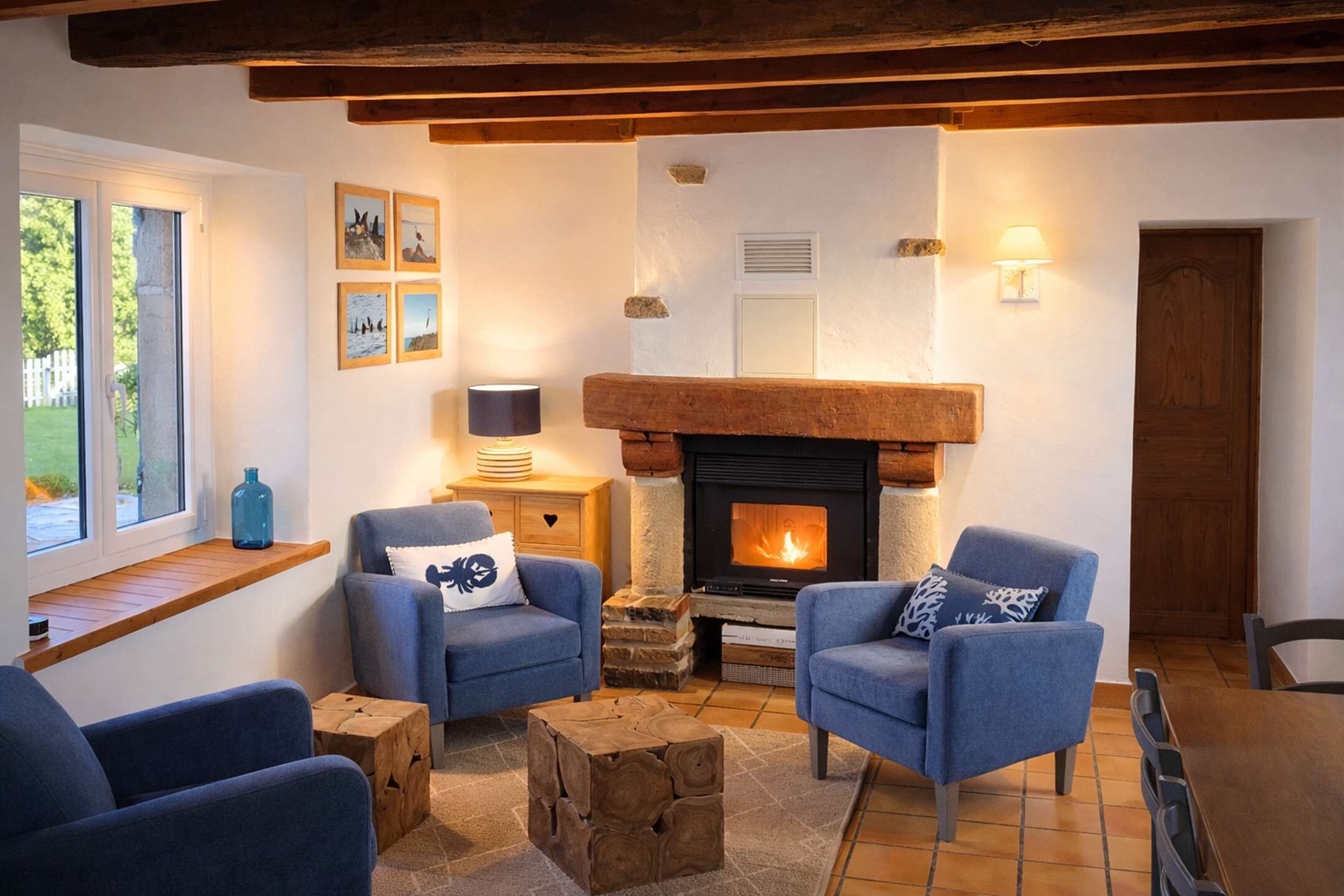 Un salon chaleureux avec une cheminée, des fauteuils bleus, une table basse en bois et une fenêtre donnant sur un beau paysage.